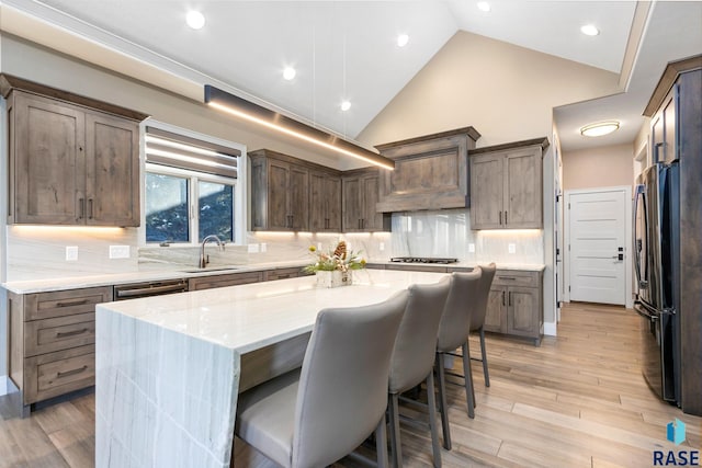 kitchen featuring high vaulted ceiling, freestanding refrigerator, a sink, light wood-style floors, and a center island