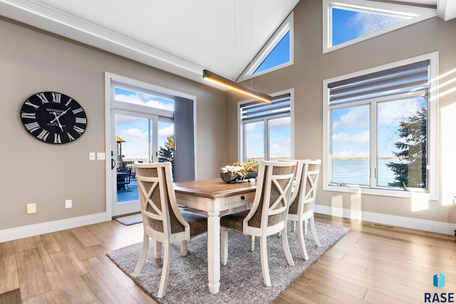 dining space with baseboards, light wood-type flooring, and high vaulted ceiling