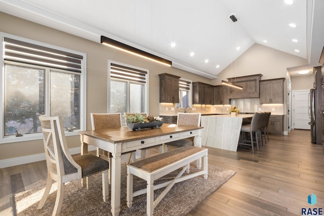 dining room with recessed lighting, light wood-style flooring, high vaulted ceiling, and baseboards