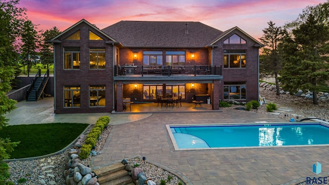 rear view of house featuring a patio area, an outdoor pool, stairs, and brick siding