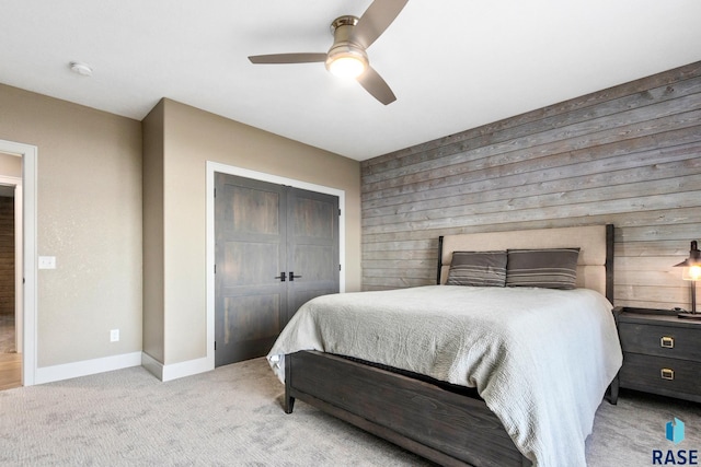 carpeted bedroom with a ceiling fan, baseboards, a closet, and wood walls