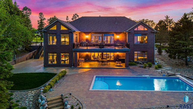 back of property at dusk featuring a balcony, stairway, a patio area, and an outdoor pool