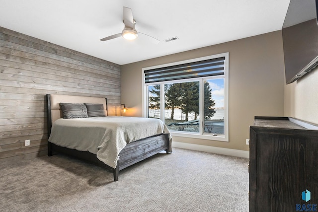 carpeted bedroom with wooden walls, baseboards, visible vents, and ceiling fan