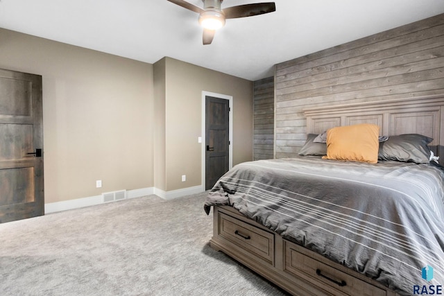 carpeted bedroom featuring a ceiling fan, baseboards, visible vents, and wood walls