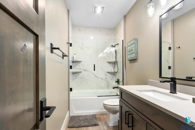 bathroom featuring visible vents, toilet, wood finished floors, bath / shower combo with glass door, and vanity