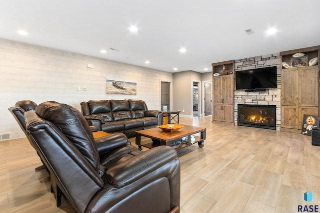 living area featuring recessed lighting, visible vents, a stone fireplace, and light wood-style flooring