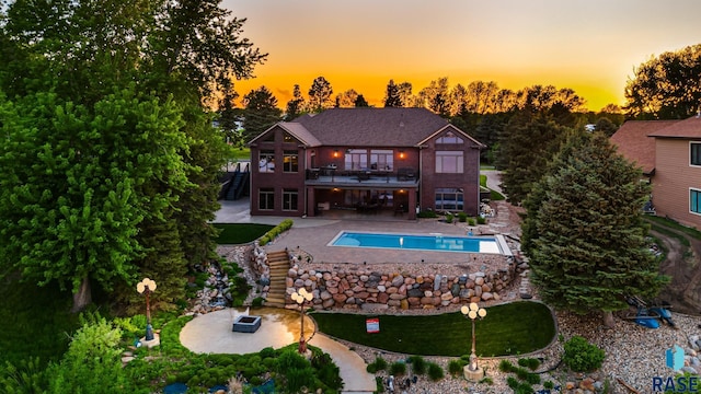 rear view of house with an outdoor pool, a patio, a balcony, and stairs