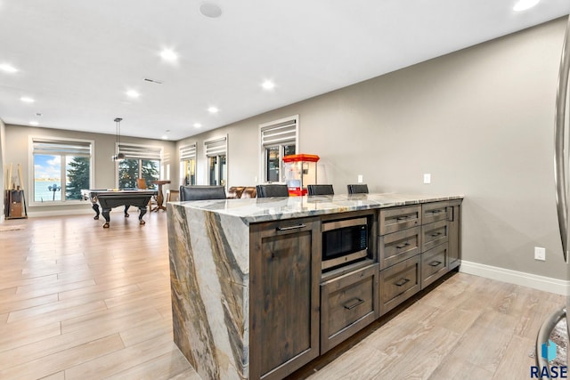 kitchen with light wood-type flooring, stainless steel microwave, recessed lighting, baseboards, and light stone countertops