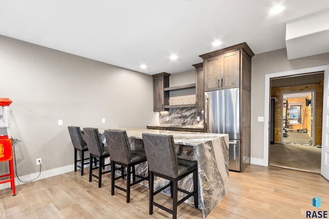 kitchen featuring a kitchen bar, stainless steel refrigerator, open shelves, light stone counters, and a peninsula