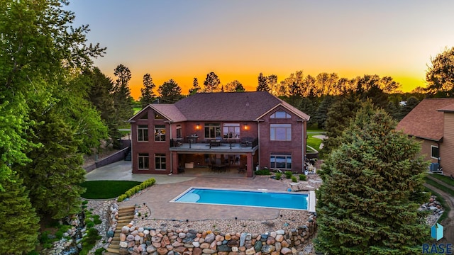 back of property at dusk featuring a patio, a balcony, and an outdoor pool