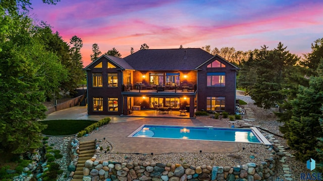 back of property at dusk with an outdoor pool, a balcony, a patio area, and fence