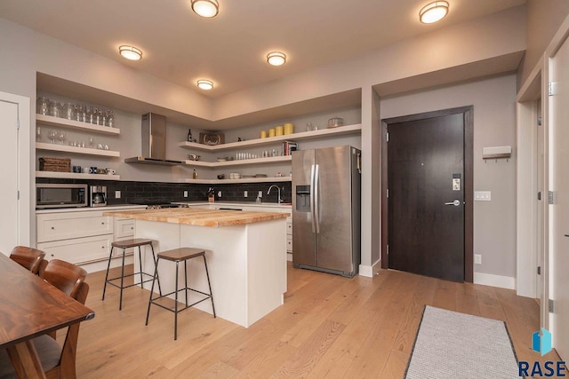 kitchen with wooden counters, wall chimney range hood, light wood-type flooring, stainless steel appliances, and open shelves