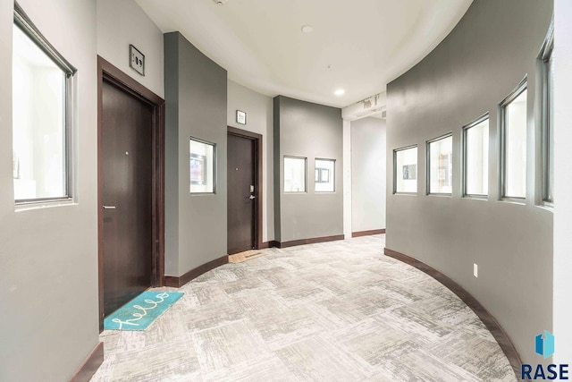 hallway featuring a healthy amount of sunlight, baseboards, and light carpet