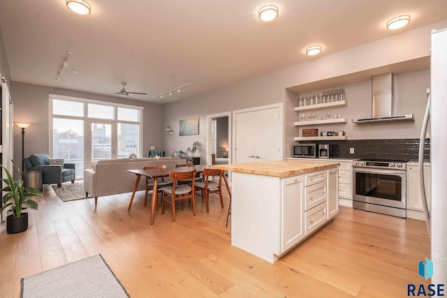 kitchen with light wood finished floors, wooden counters, appliances with stainless steel finishes, white cabinetry, and wall chimney exhaust hood