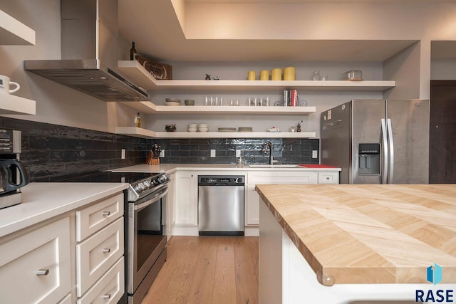 kitchen with a sink, butcher block countertops, stainless steel appliances, wall chimney exhaust hood, and open shelves