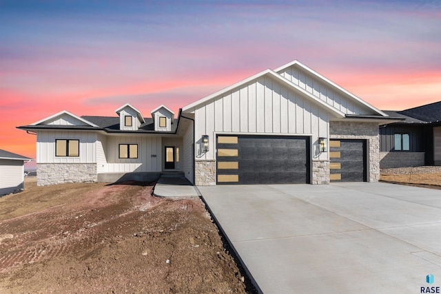 modern farmhouse style home featuring stone siding, an attached garage, concrete driveway, and board and batten siding