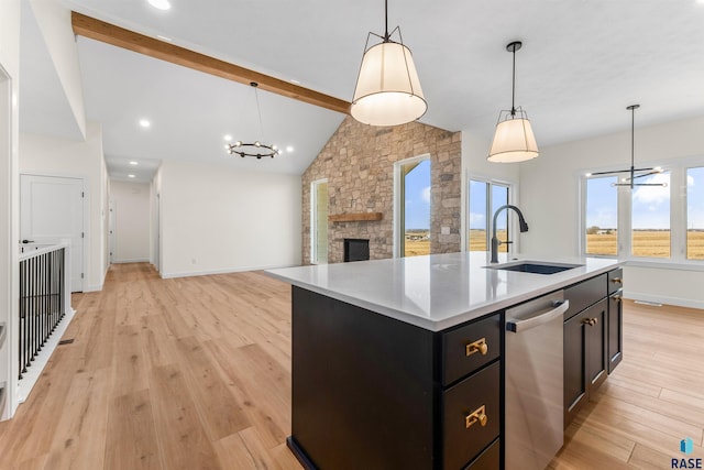 kitchen featuring beam ceiling, a sink, light wood-style floors, stainless steel dishwasher, and dark cabinets