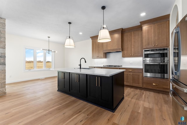 kitchen with light wood finished floors, light countertops, custom exhaust hood, stainless steel appliances, and a sink