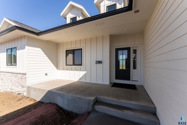 doorway to property with stone siding, board and batten siding, and visible vents