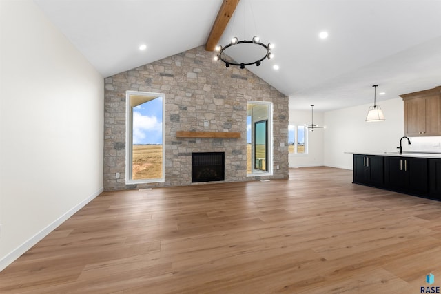 unfurnished living room with light wood-type flooring, beamed ceiling, a sink, a stone fireplace, and a chandelier