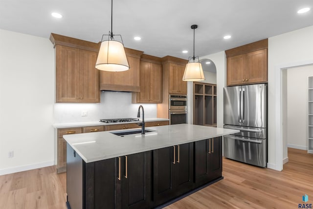 kitchen with decorative light fixtures, light wood-style flooring, stainless steel appliances, and an island with sink