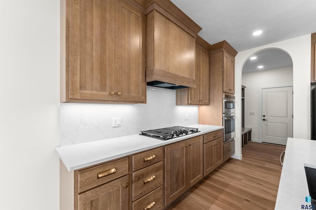 kitchen featuring gas cooktop, stainless steel double oven, light wood-style flooring, arched walkways, and light countertops