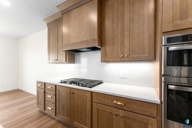 kitchen featuring double oven, black gas cooktop, light countertops, light wood-style flooring, and custom exhaust hood