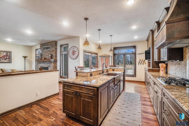 kitchen with custom range hood, dark brown cabinetry, stainless steel gas stovetop, decorative backsplash, and dark wood-style flooring