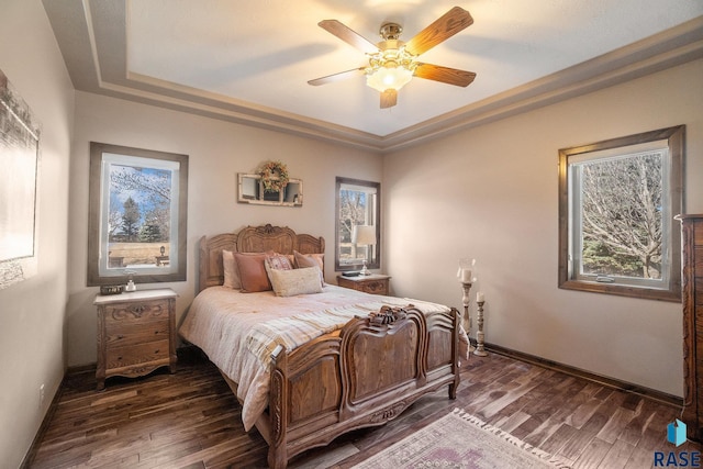 bedroom with a tray ceiling, a ceiling fan, dark wood-type flooring, and baseboards