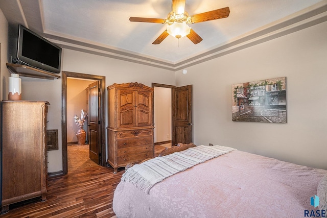 bedroom with a raised ceiling, a ceiling fan, and dark wood-style flooring