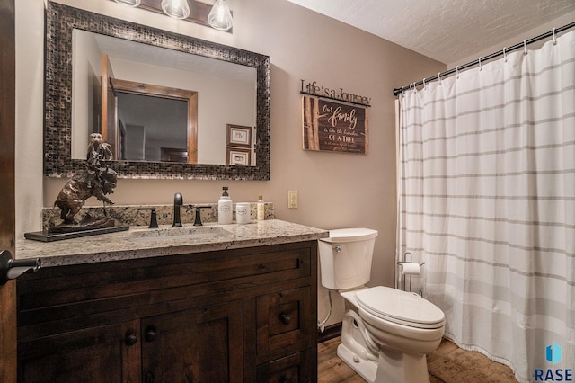 bathroom with toilet, curtained shower, a textured ceiling, wood finished floors, and vanity