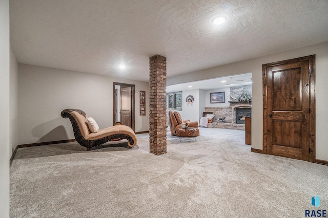 sitting room with a brick fireplace, baseboards, decorative columns, carpet flooring, and a textured ceiling