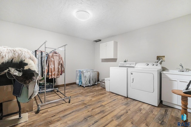 washroom featuring cabinet space, separate washer and dryer, light wood-type flooring, and a textured ceiling