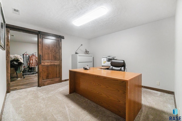 office area with light carpet, visible vents, a textured ceiling, and a barn door