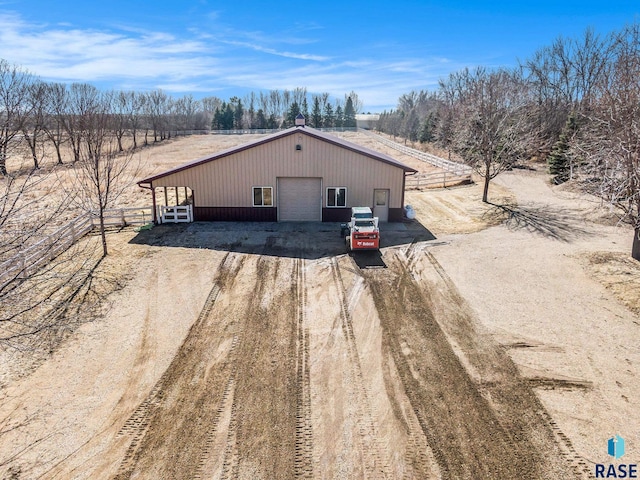 exterior space with fence, dirt driveway, a garage, a pole building, and an outbuilding