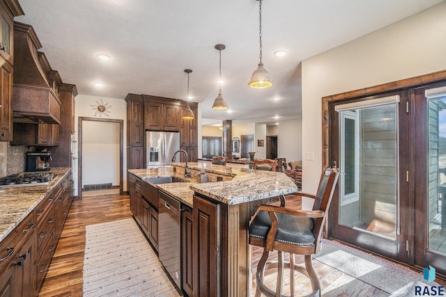 kitchen with a kitchen bar, a sink, wood finished floors, stainless steel appliances, and custom exhaust hood