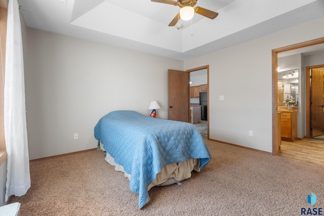 bedroom with a tray ceiling, light carpet, baseboards, and freestanding refrigerator