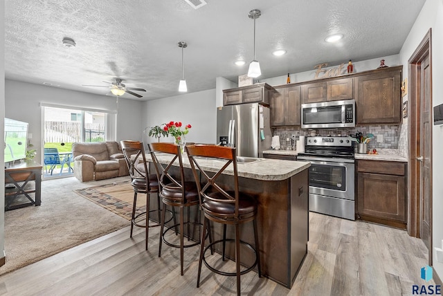 kitchen with backsplash, dark brown cabinets, open floor plan, a breakfast bar, and stainless steel appliances