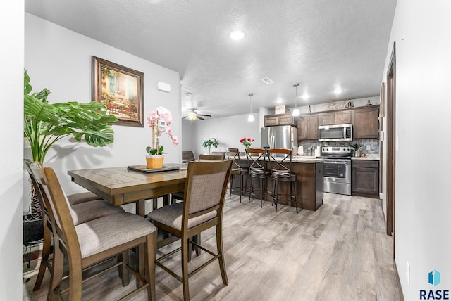 dining space featuring light wood finished floors, visible vents, a textured ceiling, and ceiling fan