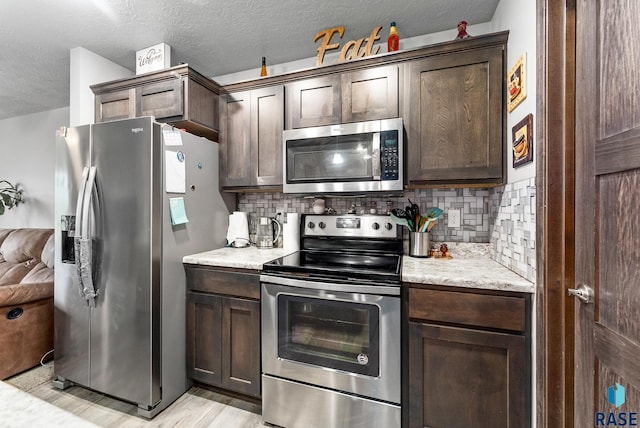 kitchen featuring tasteful backsplash, dark brown cabinets, light stone counters, stainless steel appliances, and a textured ceiling