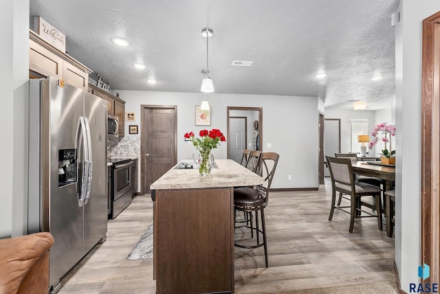 kitchen featuring backsplash, a kitchen bar, light wood-style flooring, appliances with stainless steel finishes, and a kitchen island with sink