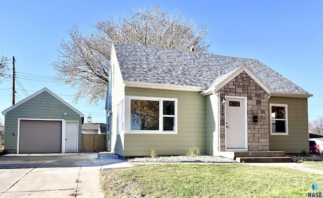 view of front of house featuring fence, roof with shingles, a front lawn, stone siding, and a detached garage