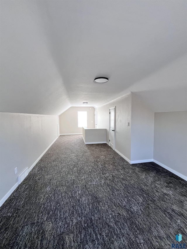 additional living space featuring visible vents, dark carpet, baseboards, and lofted ceiling