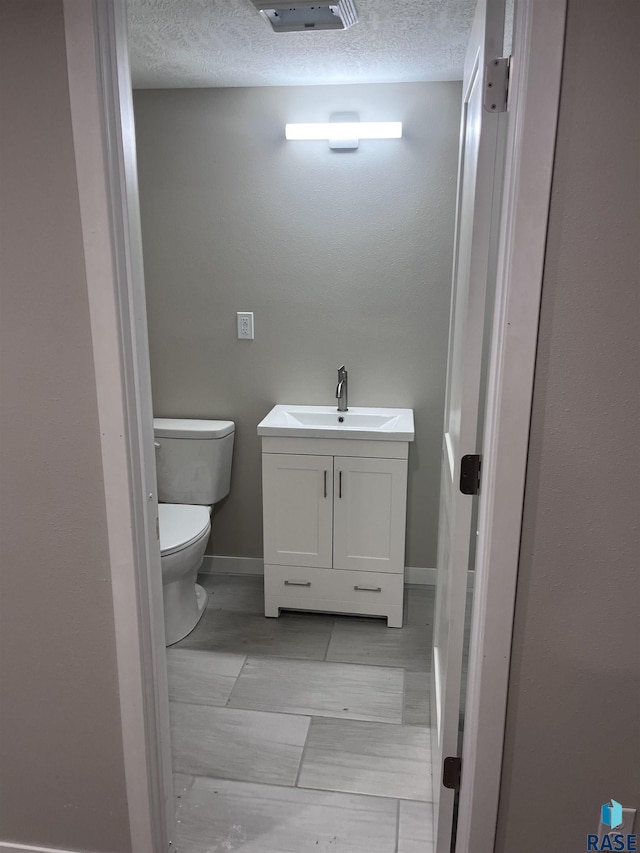 half bath featuring a textured ceiling, toilet, vanity, and baseboards