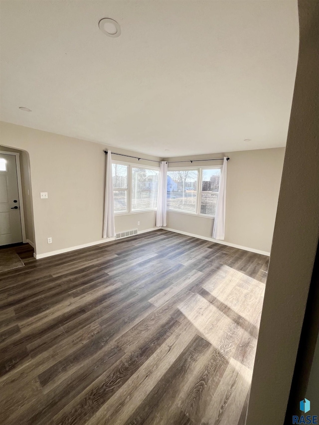 unfurnished living room featuring arched walkways, visible vents, dark wood-type flooring, and baseboards