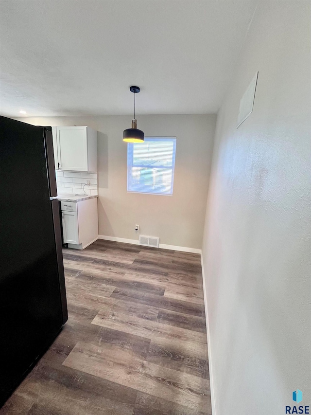 kitchen with wood finished floors, baseboards, freestanding refrigerator, white cabinetry, and backsplash