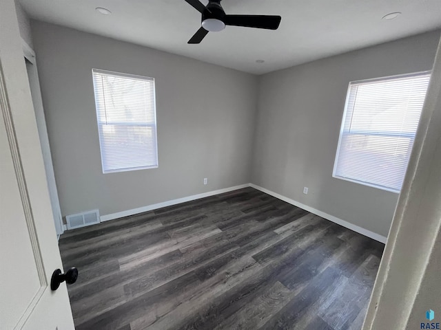 empty room featuring a wealth of natural light, visible vents, baseboards, and dark wood-style flooring