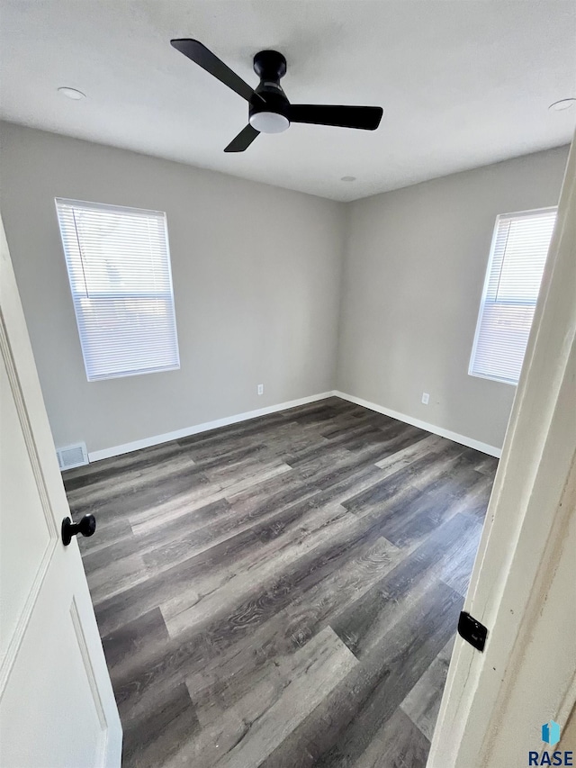 empty room featuring plenty of natural light, visible vents, and dark wood-style flooring