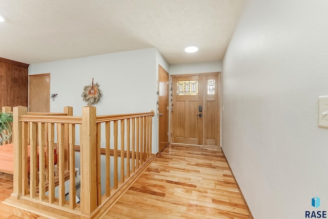 hall with an upstairs landing, a textured ceiling, and light wood-type flooring