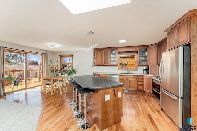 kitchen featuring a breakfast bar area, brown cabinetry, light wood-style flooring, a sink, and stainless steel appliances